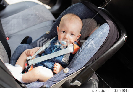 A baby boy is sitting in a baby car seat in a car. The concept of safety when transporting small children in a car, close-up 113363042