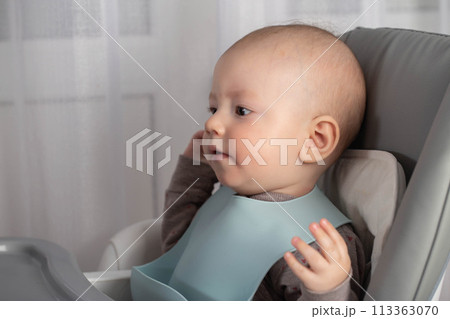 A little caucasian boy in a bib is getting ready to eat. First food for babies. Copy space for text 113363070