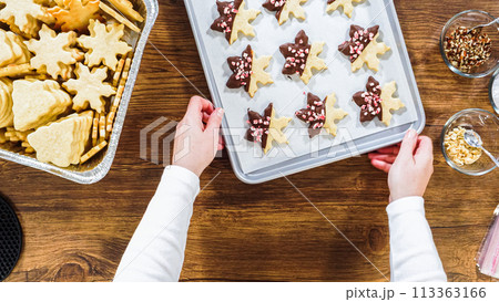 Flat lay. Carefully packaging Christmas cutout cookies, half-dipped in chocolate, sprinkled with crushed nuts, and presented in clear cellophane wrapping. 113363166
