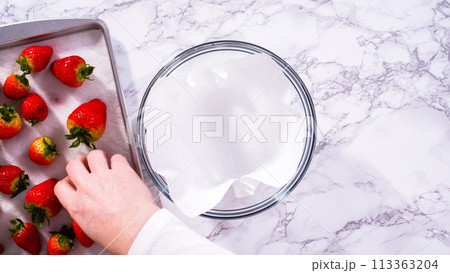 Flat lay. Strawberries, freshly washed and dried, are neatly stored in a glass bowl lined with a paper towel and securely covered with plastic wrap to maintain freshness. Flat lay. Strawberries, freshly washed and dried, are neatly stored in a glass bowl lined with a paper towel and securely covered with plastic wrap to maintain freshness. 113363204