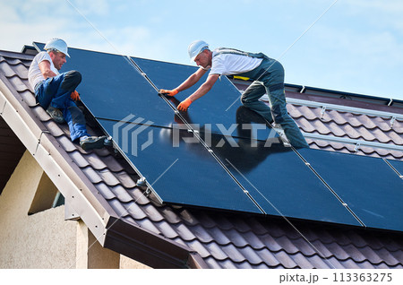 Workers building photovoltaic solar panel system on rooftop of house. Men technicians installing solar module with help of hex key outdoors. Alternative and renewable energy generation concept. 113363275