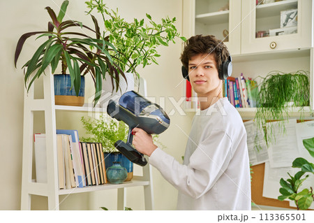 Young man wearing headphones vacuums bookshelves at home Young man wearing headphones vacuums bookshelves at home 113365501