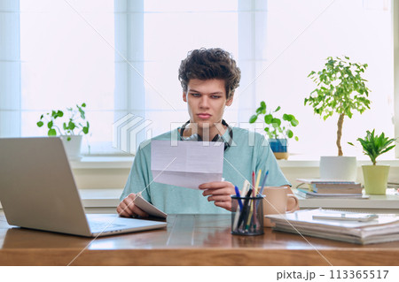 Serious young guy reading letter, paper document Serious young guy reading letter, paper document 113365517