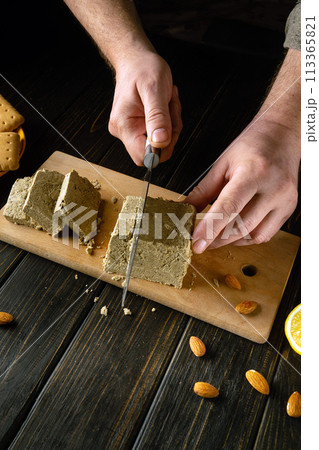 Sliced sunflower halva for dessert. A knife in the hand of a cook for cutting halva for tea with cookies and almond nuts. Advertising space 113365821