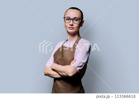 Portrait of confident serious 30s woman in apron on grey studio background Portrait of confident serious 30s woman in apron on grey studio background 113366618
