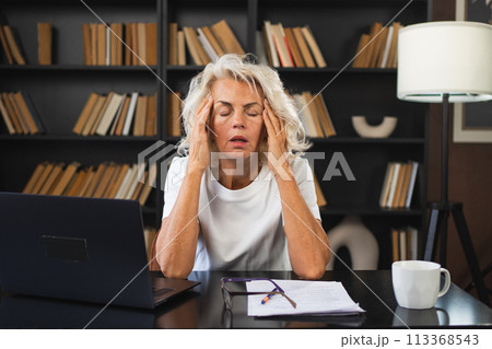 Headache pain. Middle aged woman touching temples experiencing stress. Mature old lady tired of work feeling headache sick rubbing temples forehead. Long laptop usage computer vision office syndrome Headache pain. Middle aged woman touching temples experiencing stress. Mature old lady tired of work feeling headache sick rubbing temples forehead. Long laptop usage computer vision office syndrome 113368543