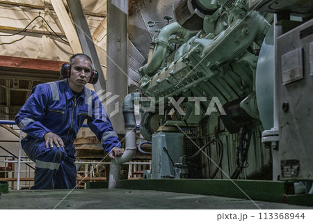 Marine Engineer in blue overall working in Engine room of ship. Work at sea. Motorman. 113368944