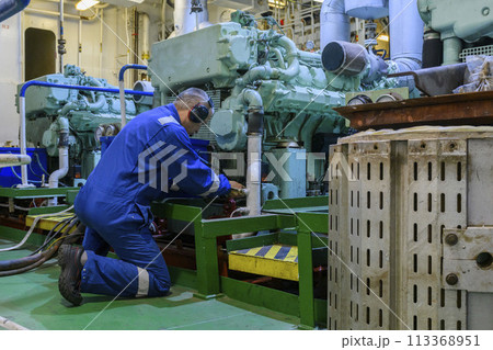 Engineer in blue overall doing service of generator in Engine room of vessel. Work at sea.  Motorman. 113368951