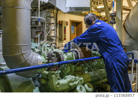 Marine Engineer in blue overall working in Engine room of ship. Work at sea. Motorman. Marine Engineer in blue overall working in Engine room of ship. Work at sea. Motorman. 113368957
