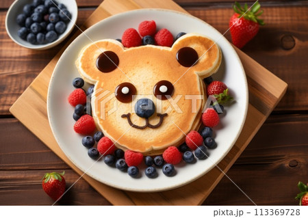 Breakfast for child, featuring bear-shaped pancakes adorned with blueberries and raspberries on white plate on wooden background 113369728