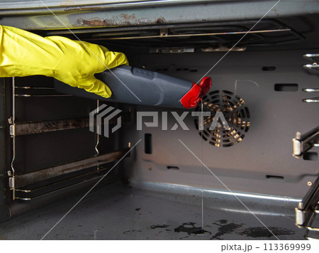 Anti-fat gel in the hand of a girl against the background of an electric oven. Care and cleaning of grease stains in the oven. Copy space for text, cleaning company 113369999