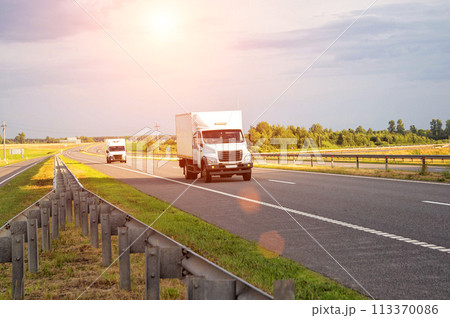 A low-tonnage commercial refrigerated van transports perishable products in the summer on a country road against the backdrop of sunset. Industry, business A low-tonnage commercial refrigerated van transports perishable products in the summer on a country road against the backdrop of sunset. Industry, business 113370086