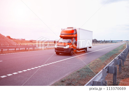 A red light-duty refrigerated van transports perishable cargo on the highway in the summer against the backdrop of sunset, industry 113370089