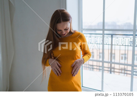 Pregnancy motherhood people expectation future. Pregnant woman with big belly standing near window at home. Girl hugging her tummy enjoying pregnancy. Maternity tenderness parenthood new life concept Pregnancy motherhood people expectation future. Pregnant woman with big belly standing near window at home. Girl hugging her tummy enjoying pregnancy. Maternity tenderness parenthood new life concept 113370105
