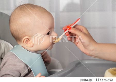 Feeding porridge and puree of a small child from a spoon. First meal. Copy space for text Feeding porridge and puree of a small child from a spoon. First meal. Copy space for text 113370258