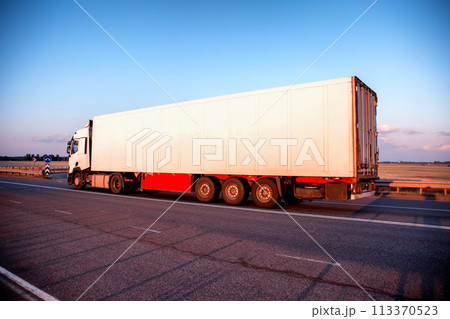 A truck with a refrigerated semi-trailer transports perishable food products in the evening against a blue sky. Import substitution, delivery of medicines, industry. 113370523