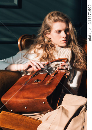 beautiful curly blond hair woman posing with a small shopper brown bag in a vintage chair beautiful curly blond hair woman posing with a small shopper brown bag in a vintage chair 113371900