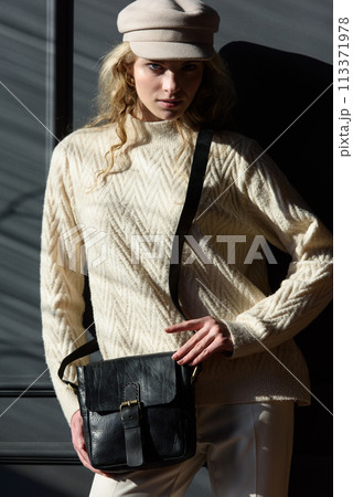 Studio portrait of beautiful woman with a curly blond hair holding black bag, posing on gray background. Studio portrait of beautiful woman with a curly blond hair holding black bag, posing on gray background. 113371978
