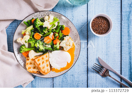 Mix of boiled vegetables, poached egg and waffle toast on a plate on the table top view 113372729