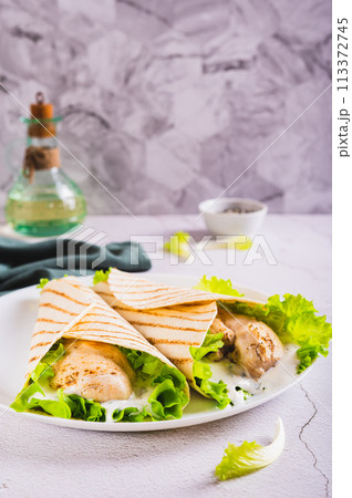 Dietary grilled tacos with chicken fillet, lettuce on a plate on the table vertical view Dietary grilled tacos with chicken fillet, lettuce on a plate on the table vertical view 113372745