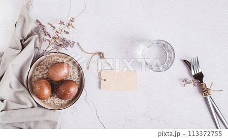 Naturally colored eggs for Easter on a plate, cutlery and a glass of water top view web banner 113372755
