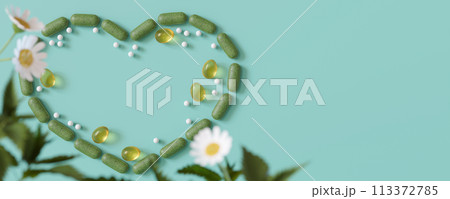 Herbal supplements and homeopathy pills artfully arranged in a heart shape with a daisy, symbolizing love for natural healthcare on blue backdrop. Homeopathic therapy. Copy space for text. Banner. 3D. 113372785