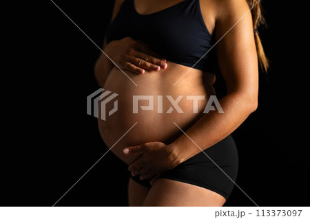 Pregnant Woman Embracing Her Belly in Dark Backdrop 113373097