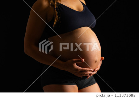 Pregnant Woman Embracing Her Belly on Black Background 113373098