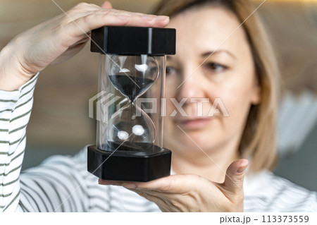 A woman holds an hourglass in front of her, looks at it. Concept of passing time. Selected Focus. High quality photo A woman holds an hourglass in front of her, looks at it. Concept of passing time. Selected Focus. High quality photo 113373559