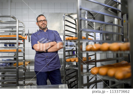 Professional man baker near fresh baked bread on tray rack trolley 113373662
