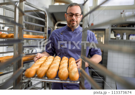 Professional man baker near fresh baked bread on tray rack trolley 113373674