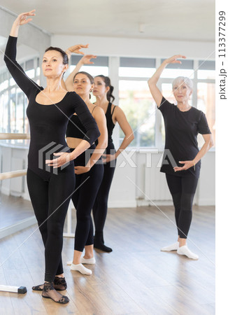 Mature teacher conducts class with girls in ballet studio, observes doing forth position exercise. Mature teacher conducts class with girls in ballet studio, observes doing forth position exercise. 113377299