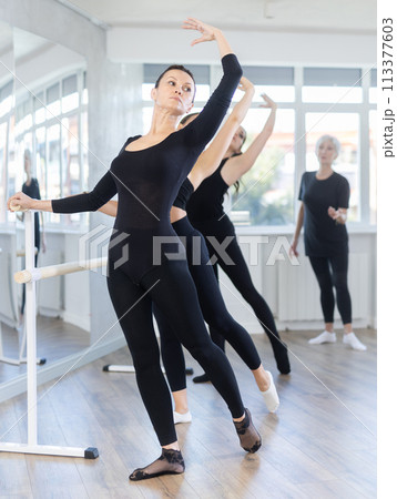 Mature teacher conducts class with girls in ballet studio, observes doing Batman exercise. Mature teacher conducts class with girls in ballet studio, observes doing Batman exercise. 113377603
