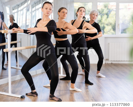 Woman practicing demi plie at barre during group ballet class 113377860