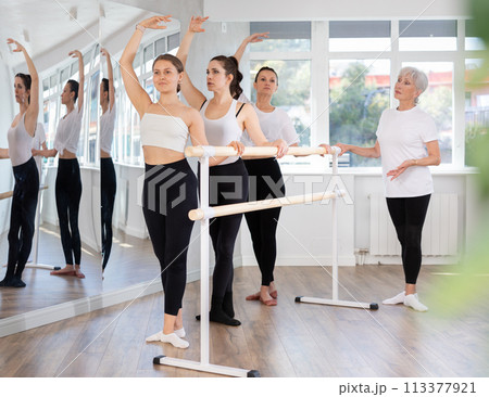 Mature teacher conducts class with girls in ballet studio, observes doing third position exercise. Mature teacher conducts class with girls in ballet studio, observes doing third position exercise. 113377921