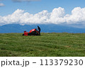 夏の高原 牧草地 赤いトラクター 草刈り機 初夏 積乱雲 113379230