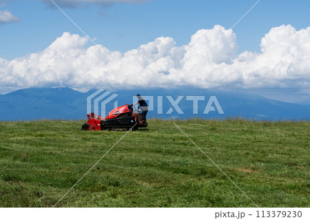 夏の高原 牧草地 赤いトラクター 草刈り機 初夏 積乱雲 113379230