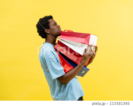Young Man Carrying Shopping Bags On Yellow Background Young Man Carrying Shopping Bags On Yellow Background 113381395