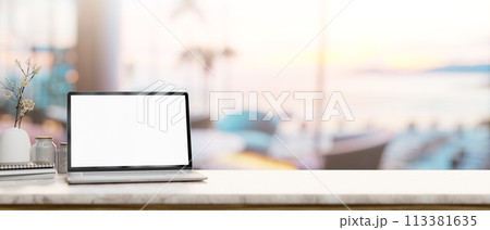 A laptop mockup on a tabletop with a blurred background of a beachfront hotel lounge or restaurant. 113381635