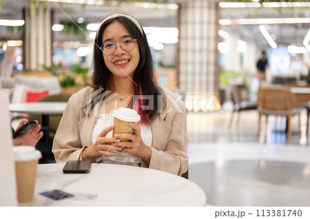 A beautiful young Asian woman in casual wear is sitting in a coffee shop in the shopping mall. A beautiful young Asian woman in casual wear is sitting in a coffee shop in the shopping mall. 113381740