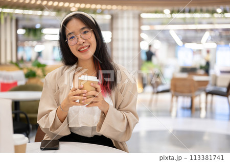 A beautiful young Asian woman in casual wear is sitting in a coffee shop in the shopping mall. 113381741