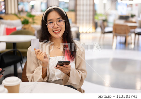 A woman is showing her credit card to the camera while sitting in a restaurant in a shopping mall. 113381743