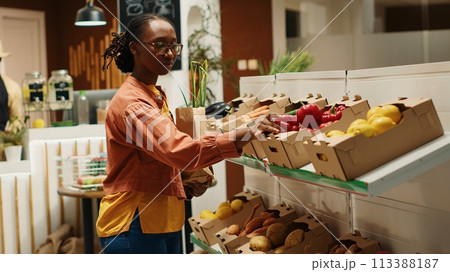 African american buyer choosing organic produce from crates, putting fruits and veggies in a paper bag to purchase. Woman shopping for natural eco friendly products at local farmers market. Camera 1. African american buyer choosing organic produce from crates, putting fruits and veggies in a paper bag to purchase. Woman shopping for natural eco friendly products at local farmers market. Camera 1. 113388187