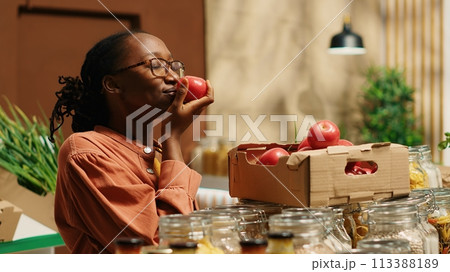 Vegan woman smelling fresh bio tomatoes from market crates, enjoying eco friendly natural aroma of locally grown produce. Regular customer choosing colorful additives free food items. Camera 1. 113388189