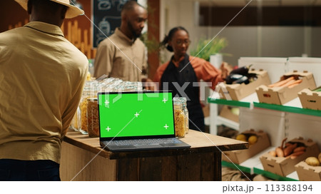 Laptop on stall at supermarket showing greenscreen template, people shopping for organic homegrown products in zero waste eco store. Portable pc with blank chromakey and copyspace. Camera 1. Laptop on stall at supermarket showing greenscreen template, people shopping for organic homegrown products in zero waste eco store. Portable pc with blank chromakey and copyspace. Camera 1. 113388194