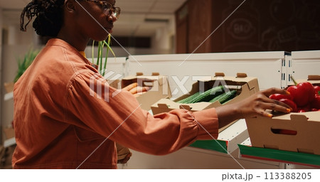 African american buyer choosing organic produce from crates, putting fruits and veggies in a paper bag to purchase. Woman shopping for natural eco friendly products at local farmers market. Camera 2. 113388205