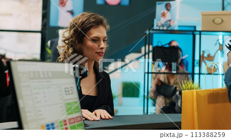 African american retail clerk scanning barcode on bag at cash register, preparing items for customer at department store. Young woman choosing trendy accessories from showroom. Camera A. 113388259