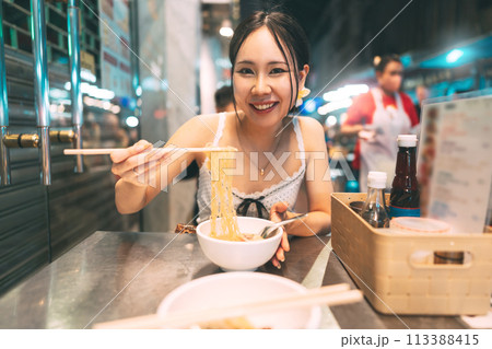 Asian foodie tourist woman eating wonton noodles at China town asia street food night market Asian foodie tourist woman eating wonton noodles at China town asia street food night market 113388415