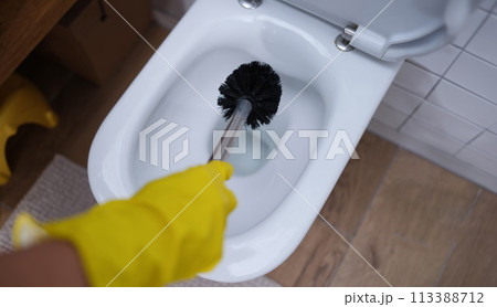 Gloved hand is cleaning toilet with brush closeup 113388712