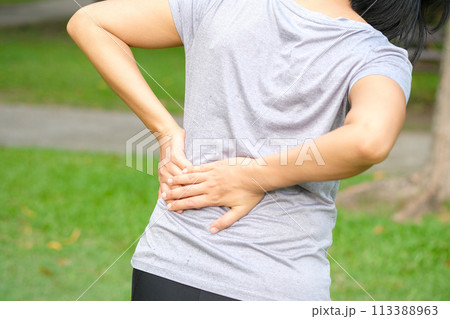 Woman's hand She is caught at the waist and her back is painful at the back in the park. Cause of the exercise. 113388963